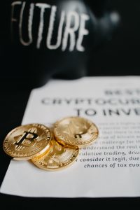 Alcancía con forma de cochino con la palabra Future a un lado puesto sobre una hoja de papel junto a tres monedas de Bitcoins físicas